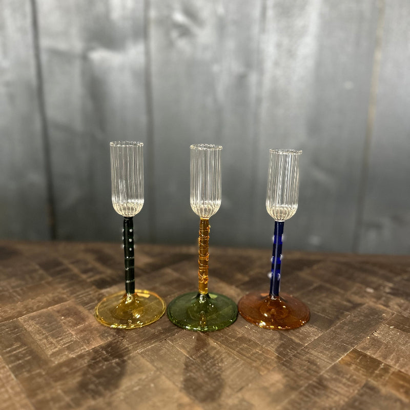 Three decorative glass goblets with colored stems on a textured surface.