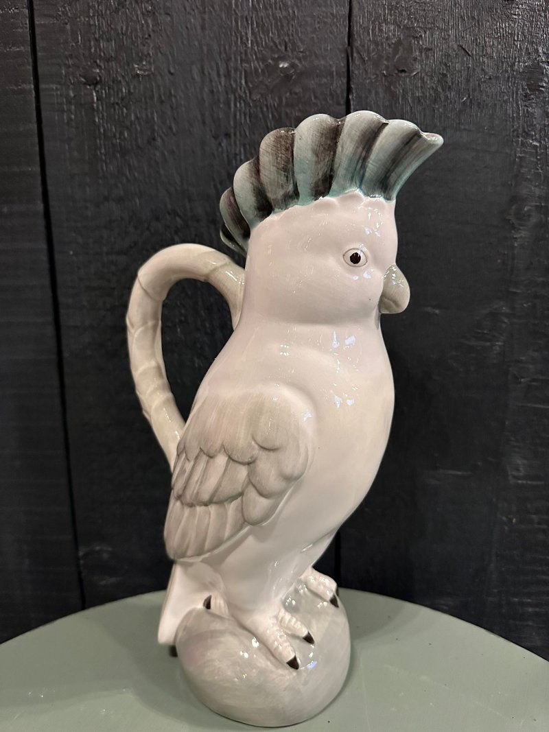 A ceramic cockatoo-shaped jug with a gray body and a green tufted head, perched on a round base.