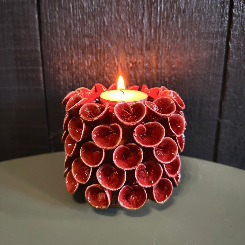 A cranberry red ceramic tealight holder with a textured design, containing a lit tealight candle, placed on a dark surface.