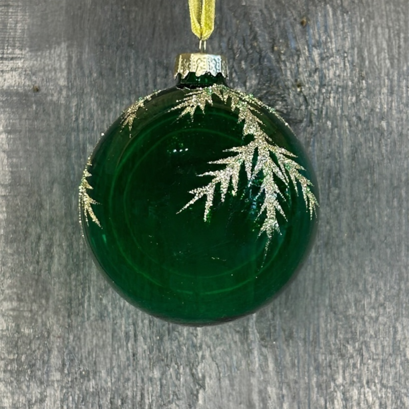 Green glass ornament with gold leaf design on a gray surface