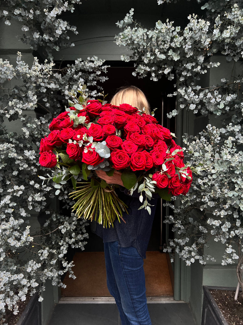A person holding a large bouquet of red roses with foliage, arranged and wrapped for gift-giving.