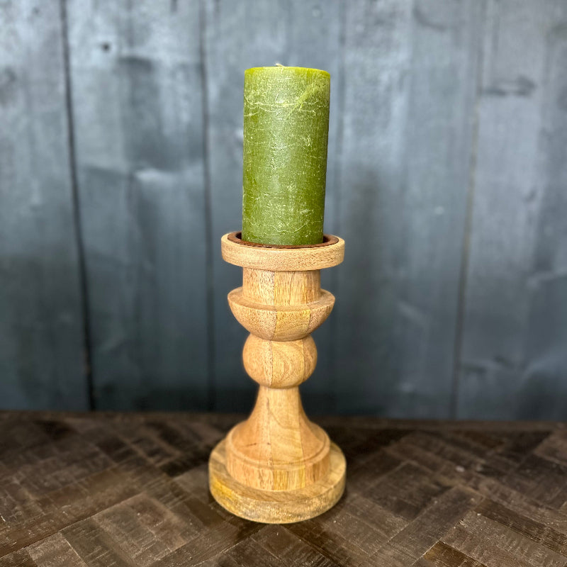 Green candle in a wooden holder on a textured surface with a gray wooden panel background