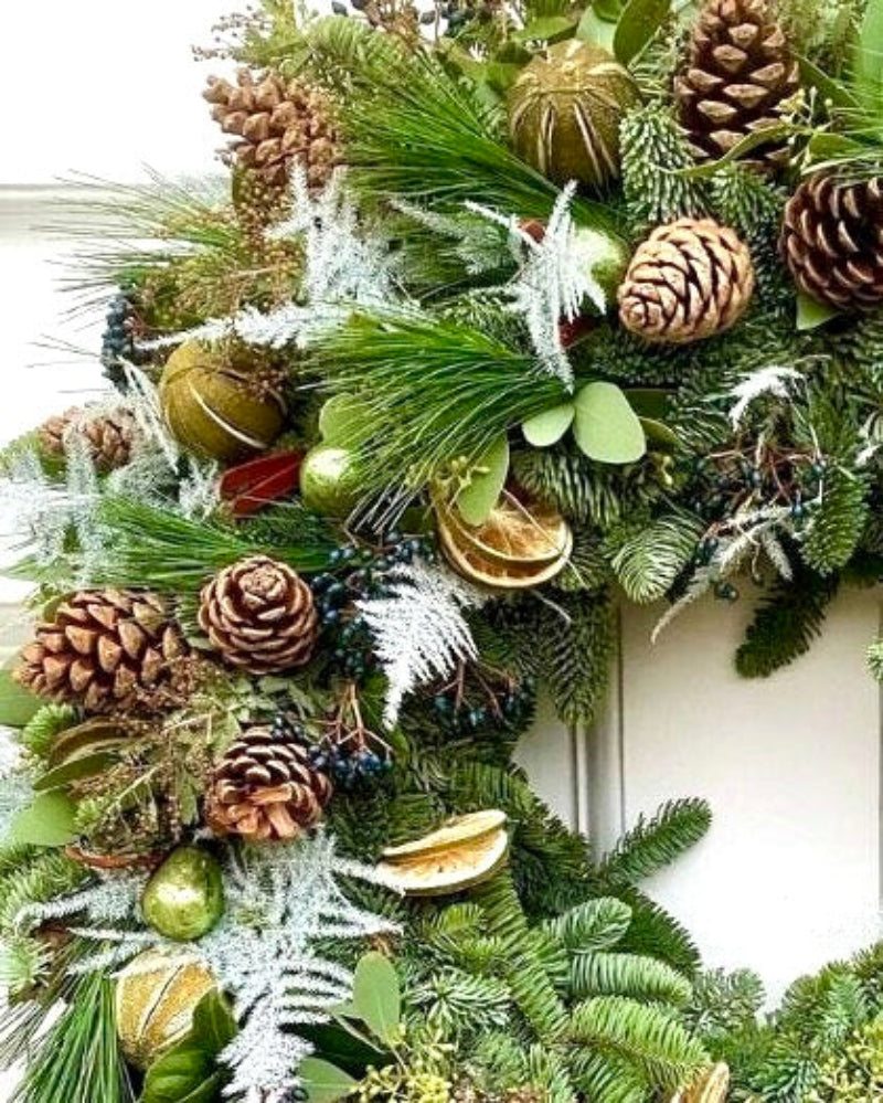 Decorative Christmas wreath with greenery, pinecones, and ornaments on a white background