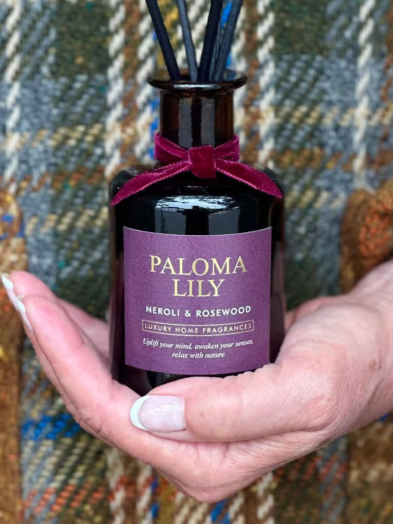 Bottle of Paloma Lily home fragrance held in a hand with a textured fabric background