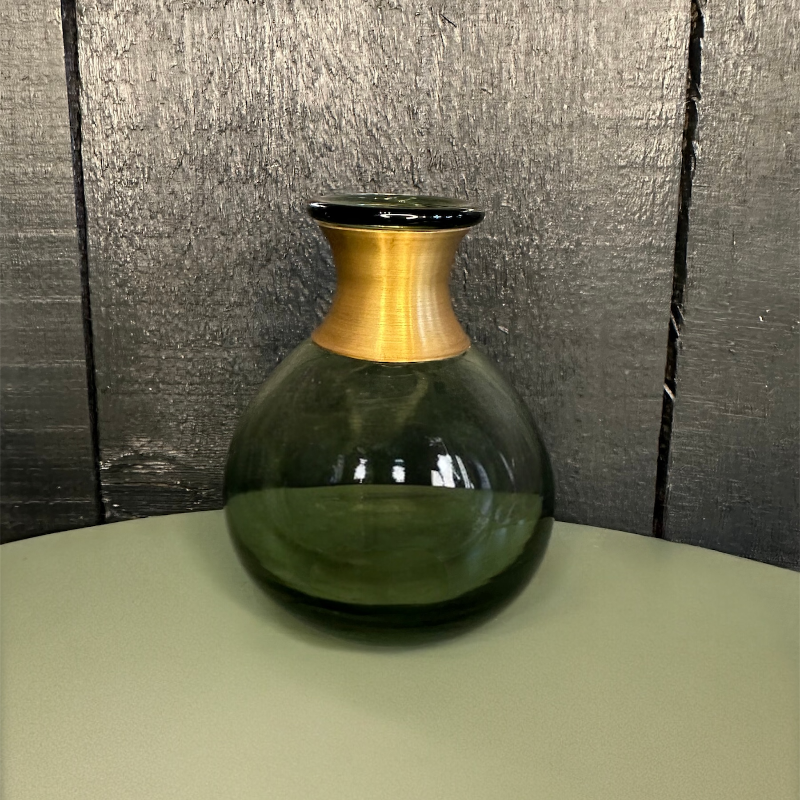 Green glass vase with gold accent on a neutral surface with textured gray background