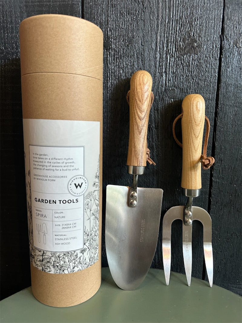 A pair of gardening tools with stainless steel heads and wooden handles, displayed next to their packaging tube which has &