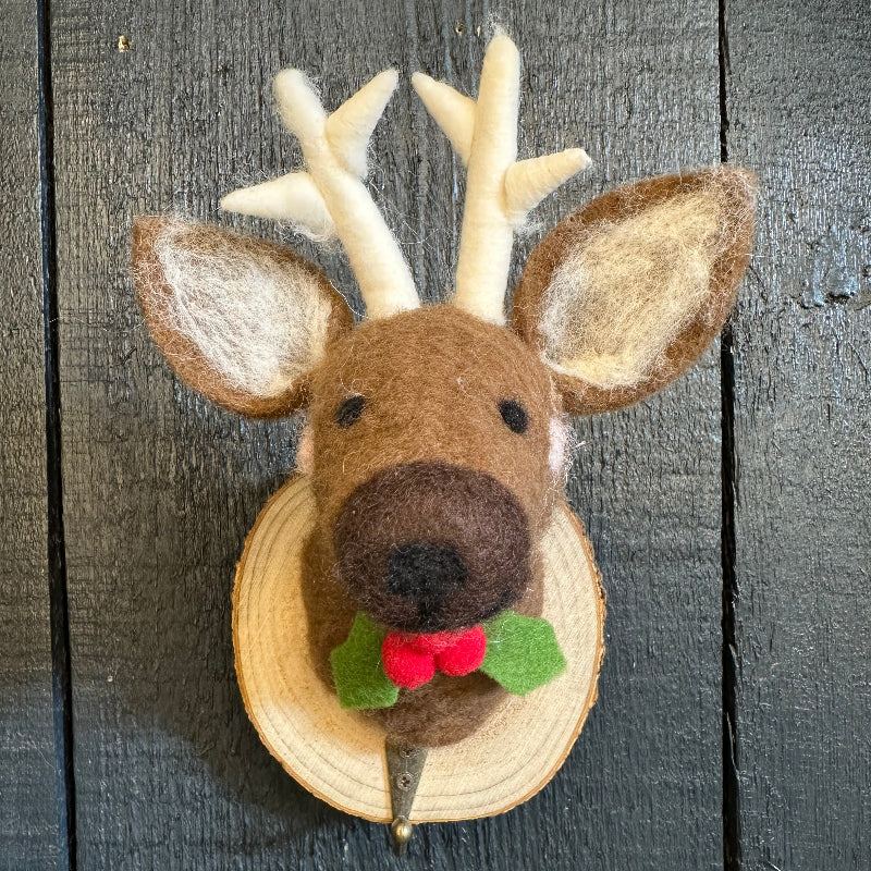 Felt reindeer decoration with antlers and a holly berry on a wooden surface