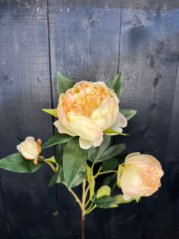 Artificial flower arrangement with peach-colored flowers and green leaves on a dark wooden background