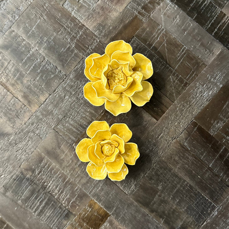 Two yellow ceramic flowers on a textured gray surface