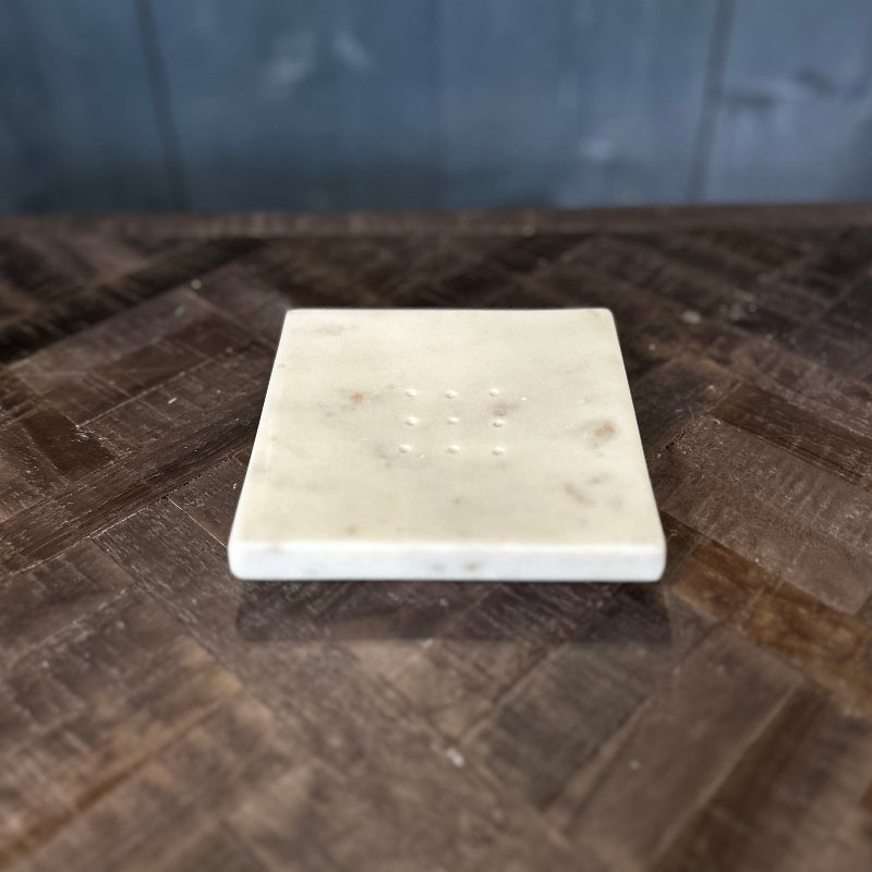 Square marble coaster on a wooden surface with a blurred blue tiled wall in the background