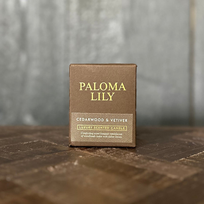 Paloma Lily cedarwood & vetiver scented candle packaging on a wooden surface with a blurred background