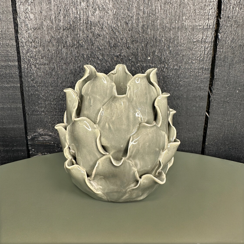 Ceramic artichoke-shaped tealight holder on a flat surface with a textured wall background