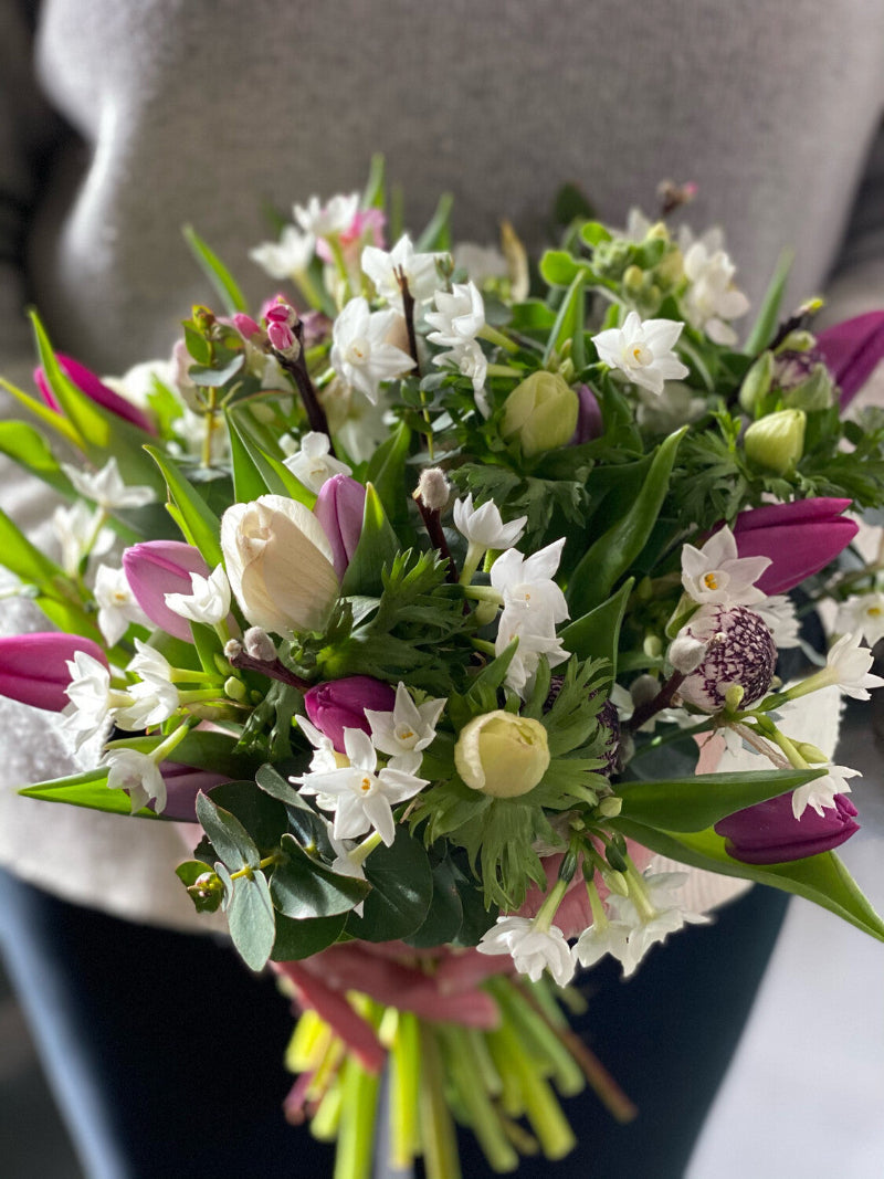 A bouquet of seasonal spring flowers including tulips, ranunculus, and cherry blossoms, arranged and wrapped with velvet trim and a handwritten personal message.