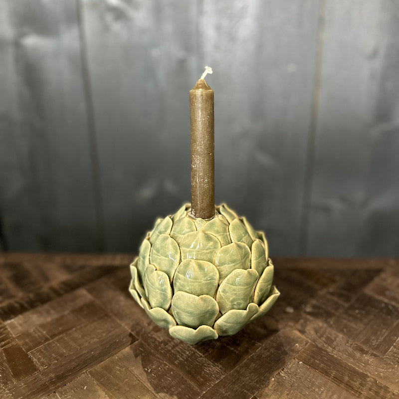 Candle holder shaped like an artichoke with a lit candle on a wooden surface.