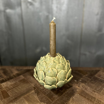 Candle holder shaped like an artichoke with a lit candle on a wooden surface.