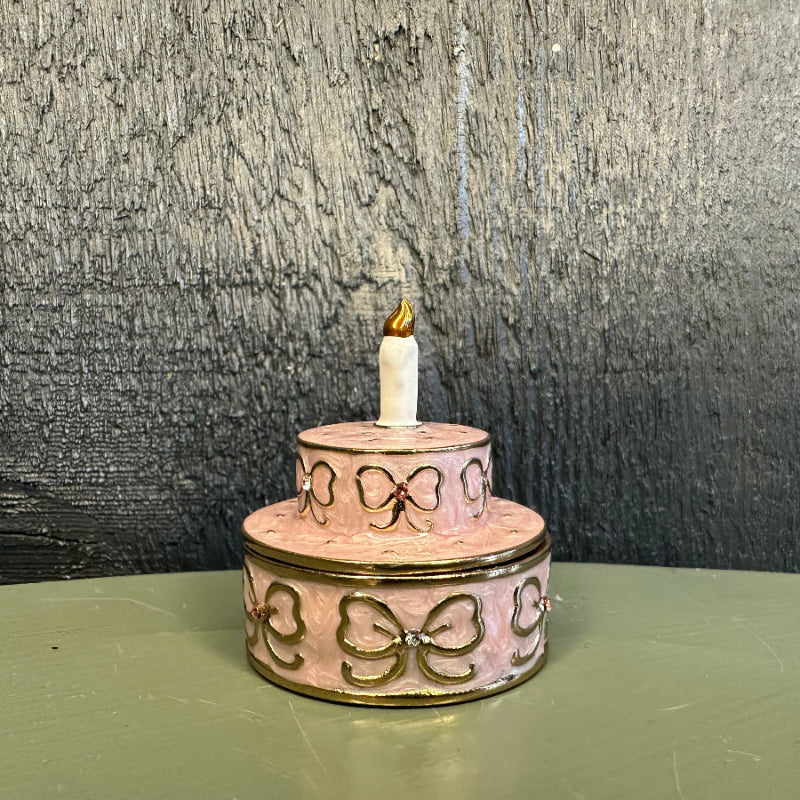 Two-tiered decorative cake with a candle on a green surface against a textured gray background