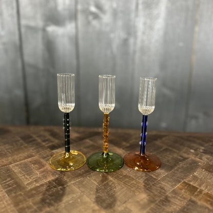 Three decorative glass goblets with colored stems on a textured surface.