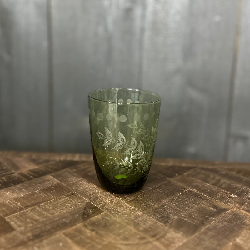 Green glass tumbler with leaf patterns on a wooden surface and gray background