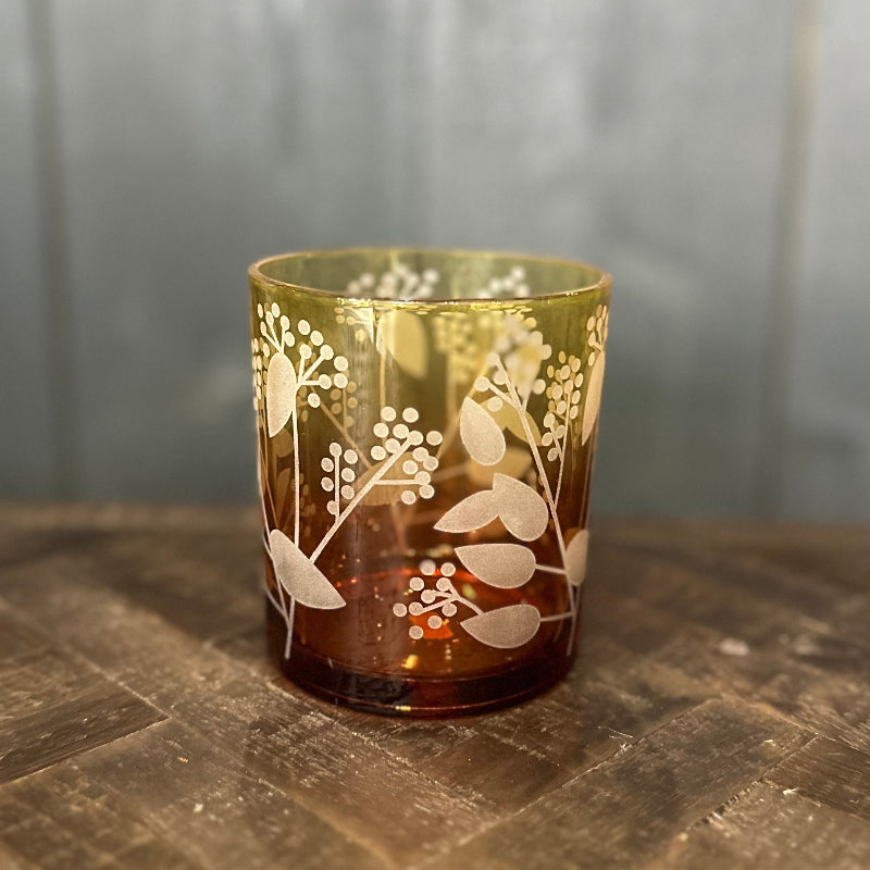 Decorative glass candle holder with floral patterns on a wooden surface.