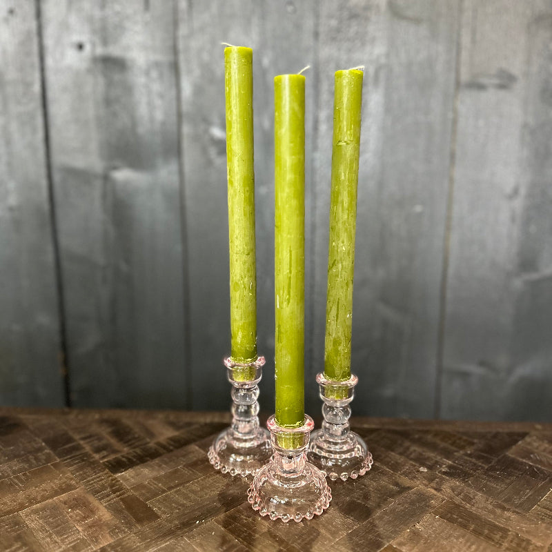 Three green candles in decorative candle holders on a wooden surface with a gray wooden background.
