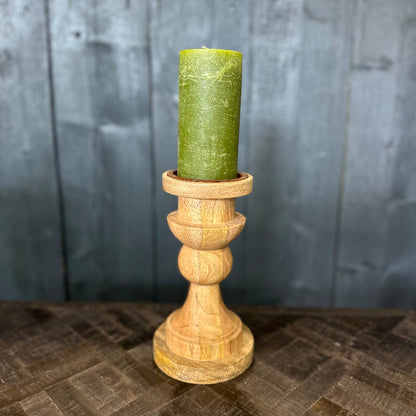 Green candle in a wooden holder on a textured surface with a gray wooden panel background