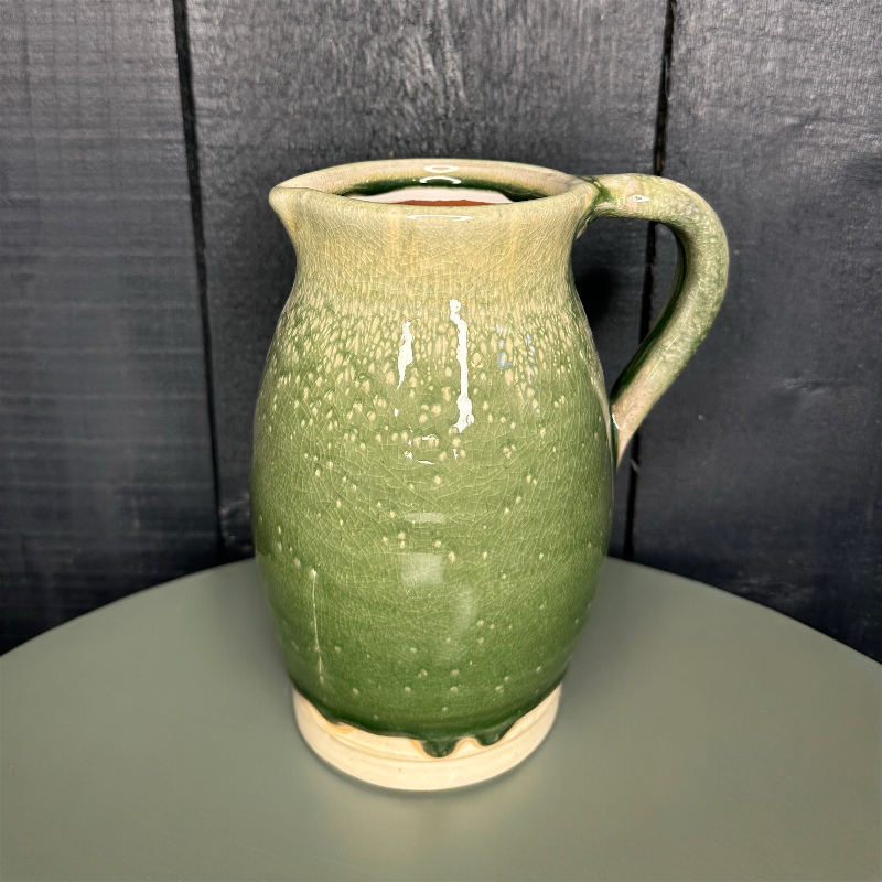 Green ceramic pitcher on a gray surface with a dark textured wall background