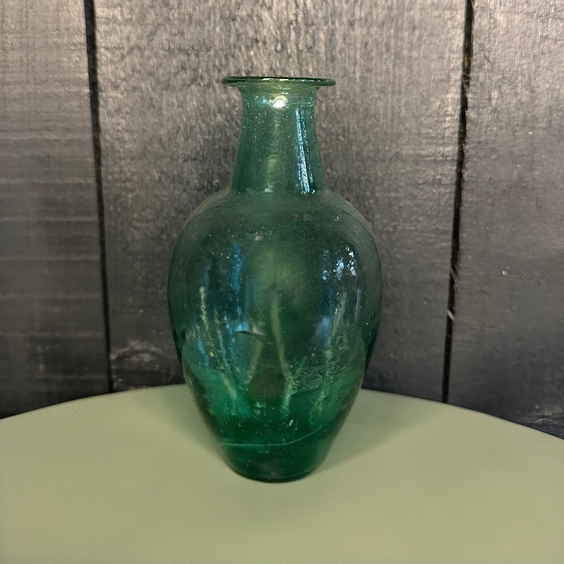 Green glass vase on a round surface with a dark textured background