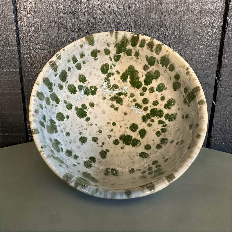 Ceramic bowl with green speckled pattern on a wooden surface