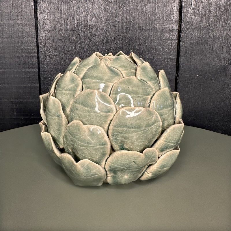Decorative ceramic artichoke on a dark surface with a dark wooden background