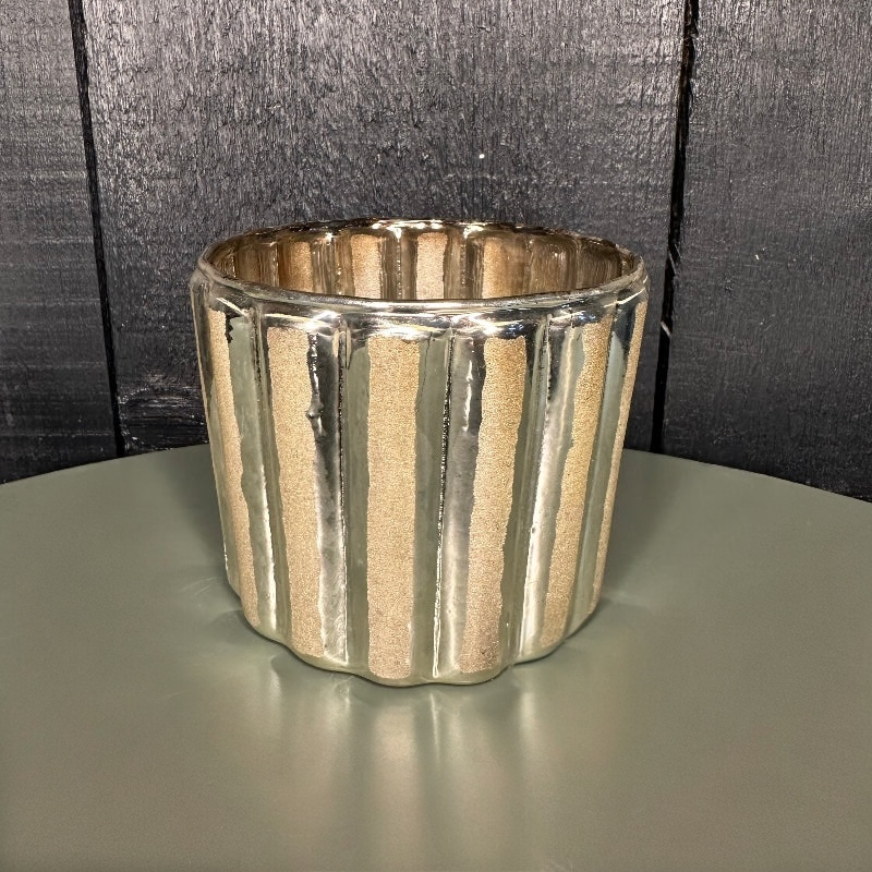 Silver ribbed candle holder on a dark surface with a dark background
