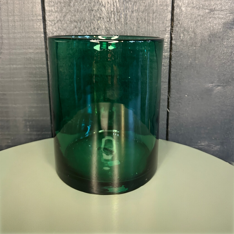 Green glass vase on a round surface with a textured gray wall background