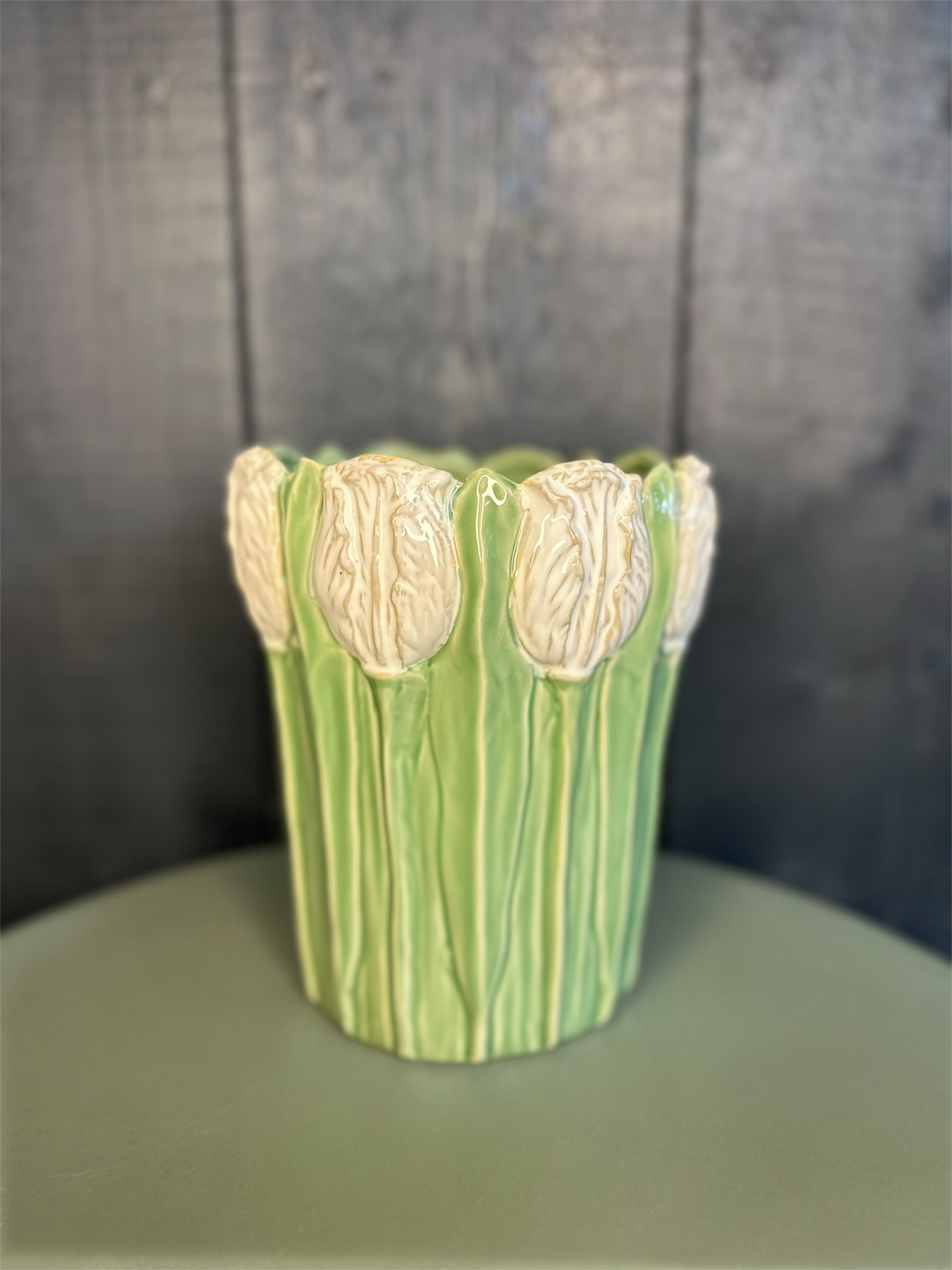 Green ceramic vase with floral design on a gray background