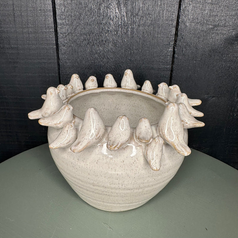 Ceramic vase with bird-like figures around its rim on a dark background