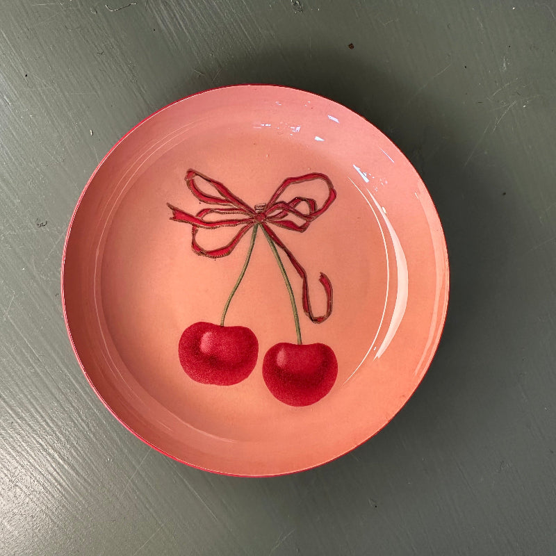 Pink plate with red cherries and a bow on a gray surface