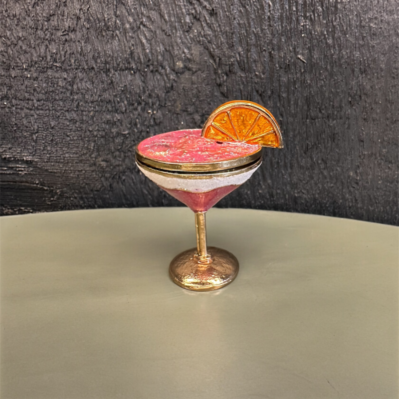 Cocktail with a pink rim and orange slice garnish on a dark background