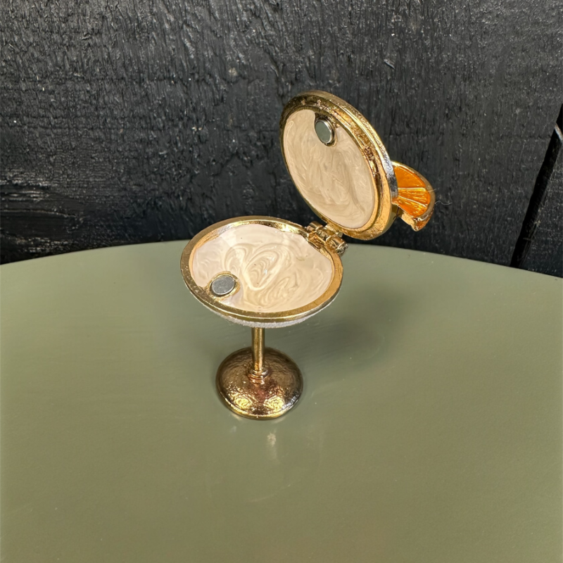 Decorative item resembling a miniature jewelry stand with open lid on a green surface.