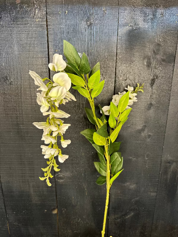 Artificial flower branch with white flowers and green leaves on a dark wooden background