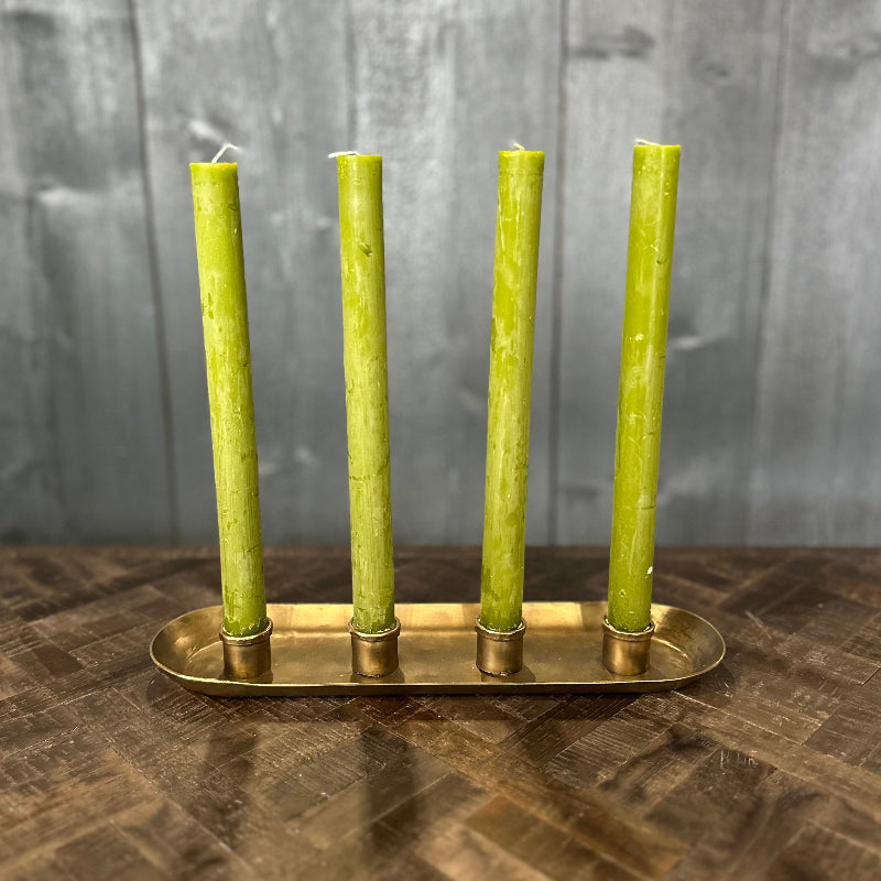 Four green candles in a brass candle holder on a wooden surface with a gray background