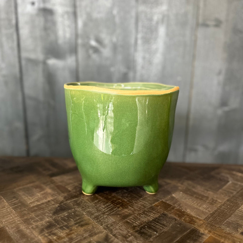 Green ceramic pot on a wooden surface with a gray wooden panel background