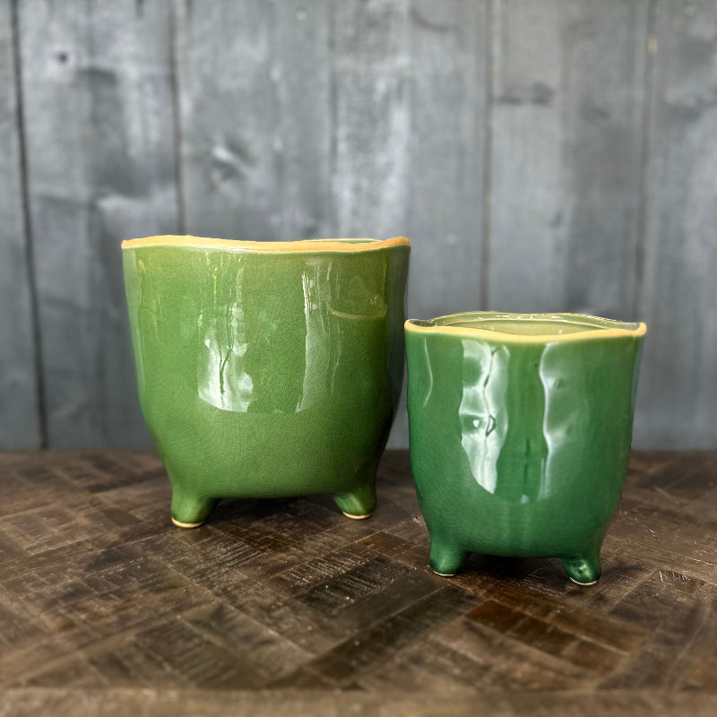 Two green ceramic pots on a wooden surface with a gray wooden panel background