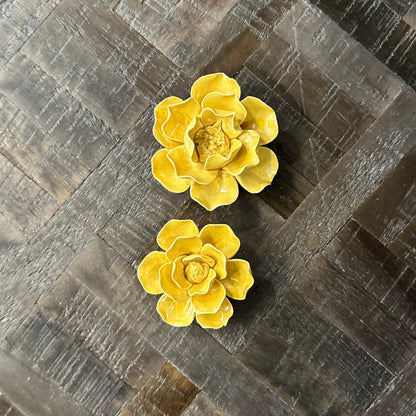 Two yellow ceramic flowers on a textured gray surface