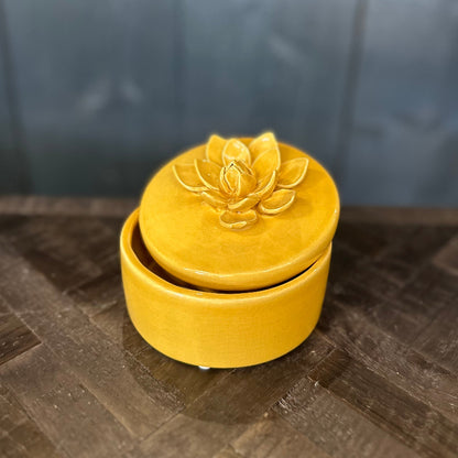 Yellow ceramic container with lotus flower design on a textured surface