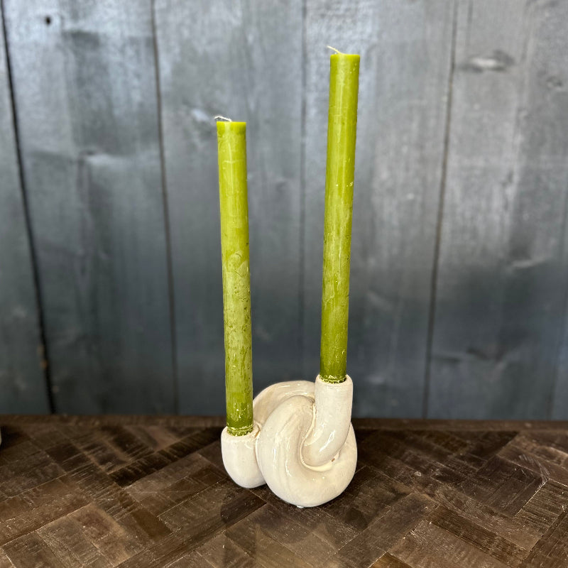 Two green candles in a white ceramic holder on a wooden surface with a gray wooden panel background.