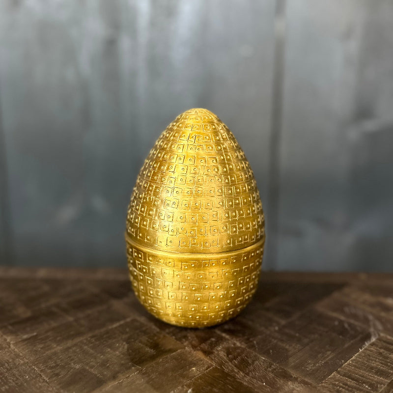 Gold textured egg-shaped object on a dark surface with a gray background