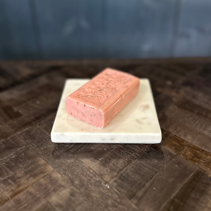 Rectangular pink bar of soap on a white marble slab with a dark wooden background