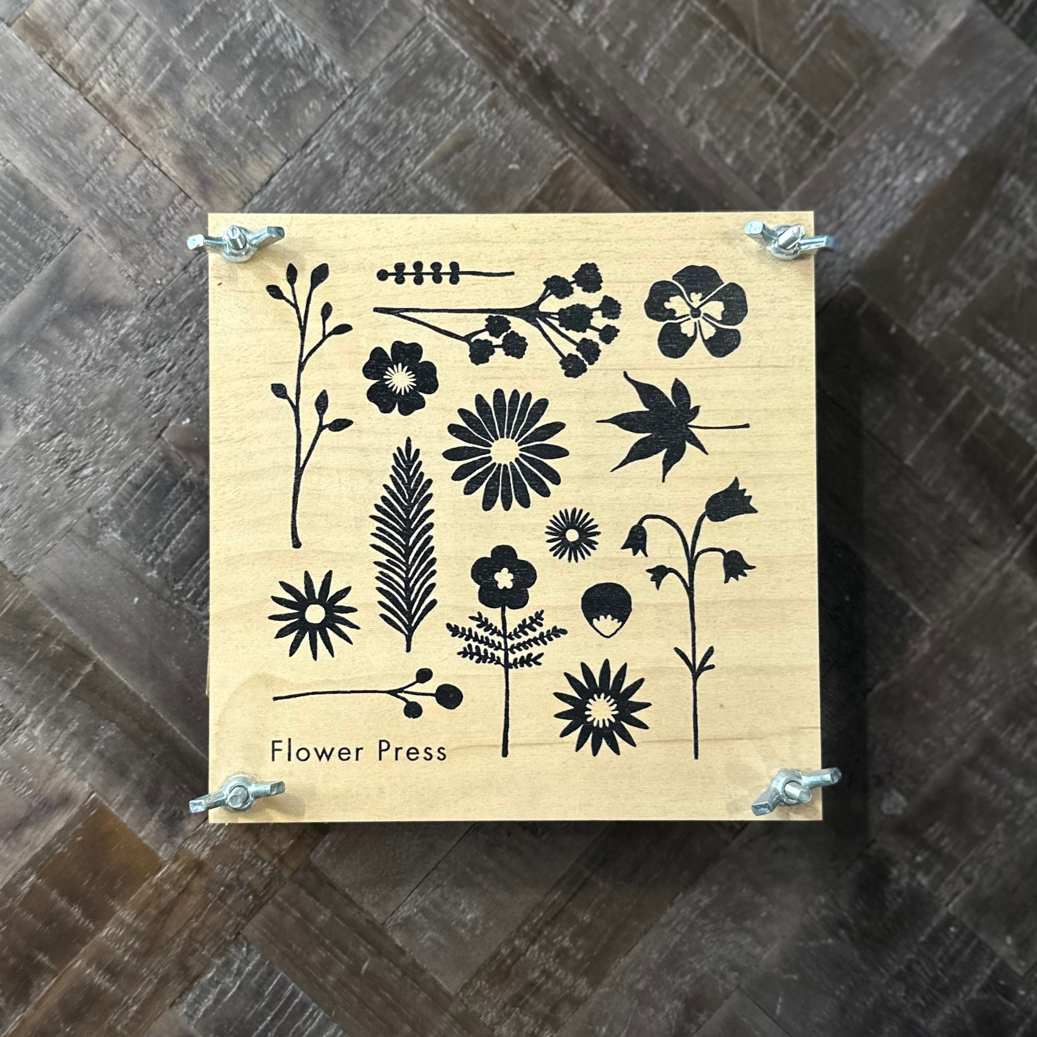 Wooden flower press with black floral designs on a wooden surface