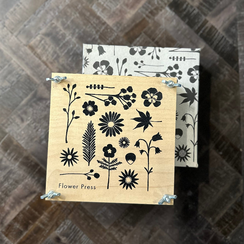 Wooden flower press with black floral designs on a wooden surface