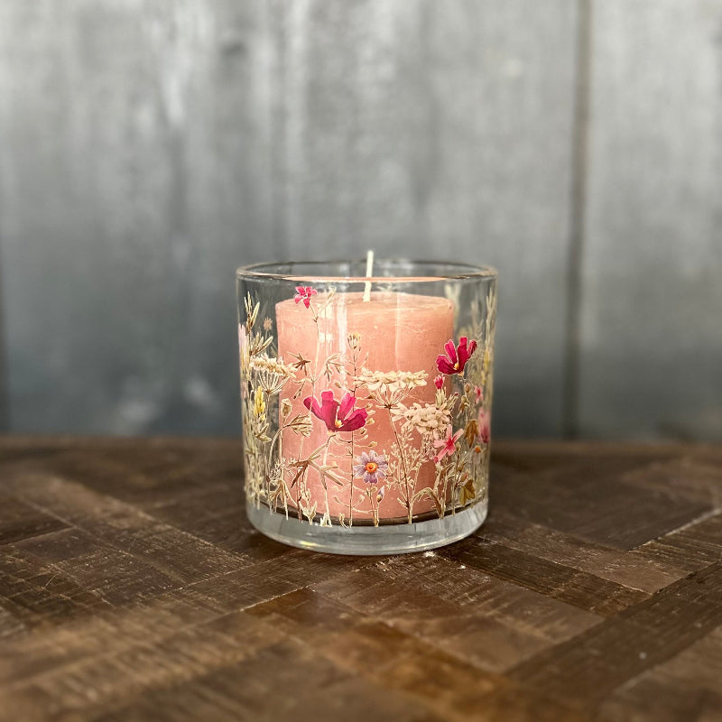 Pink candle in a glass holder with floral design on a wooden surface