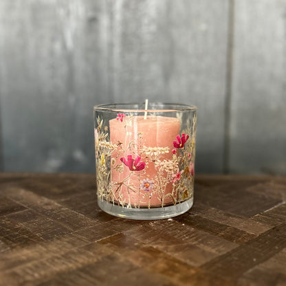 Pink candle in a glass holder with floral design on a wooden surface