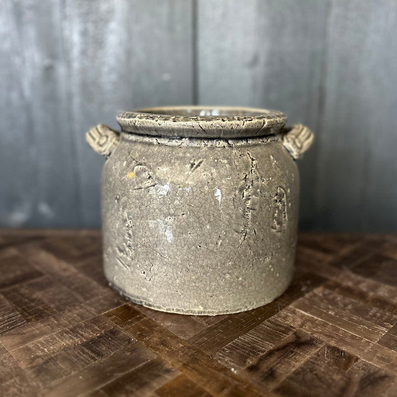 Vintage-style gray pot with decorative handles on a wooden surface and gray background
